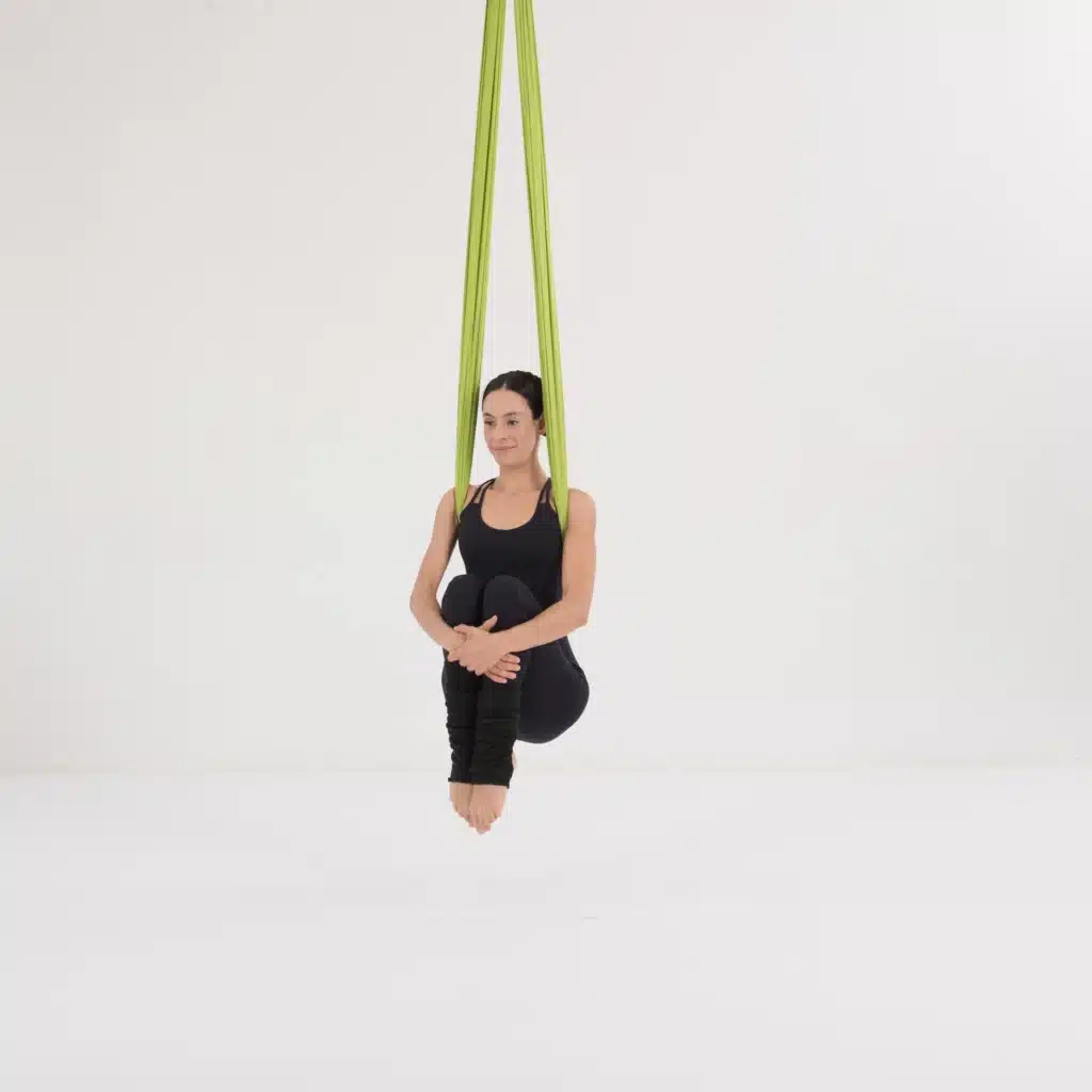 Aerial Yoga Kanonenkugel im Aerial Yoga Tuch. Frau zieht die Knie zur Brust für ein intensives Bauchtraining und Core Aktivierung im Yoga Hammock.