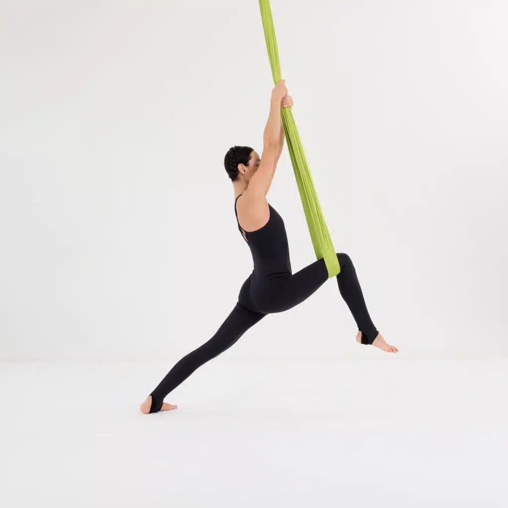 Aerial Yoga Krieger 2 im Tuch mit stabilem Ausfallschritt und aktiv gehobenem Oberkörper.