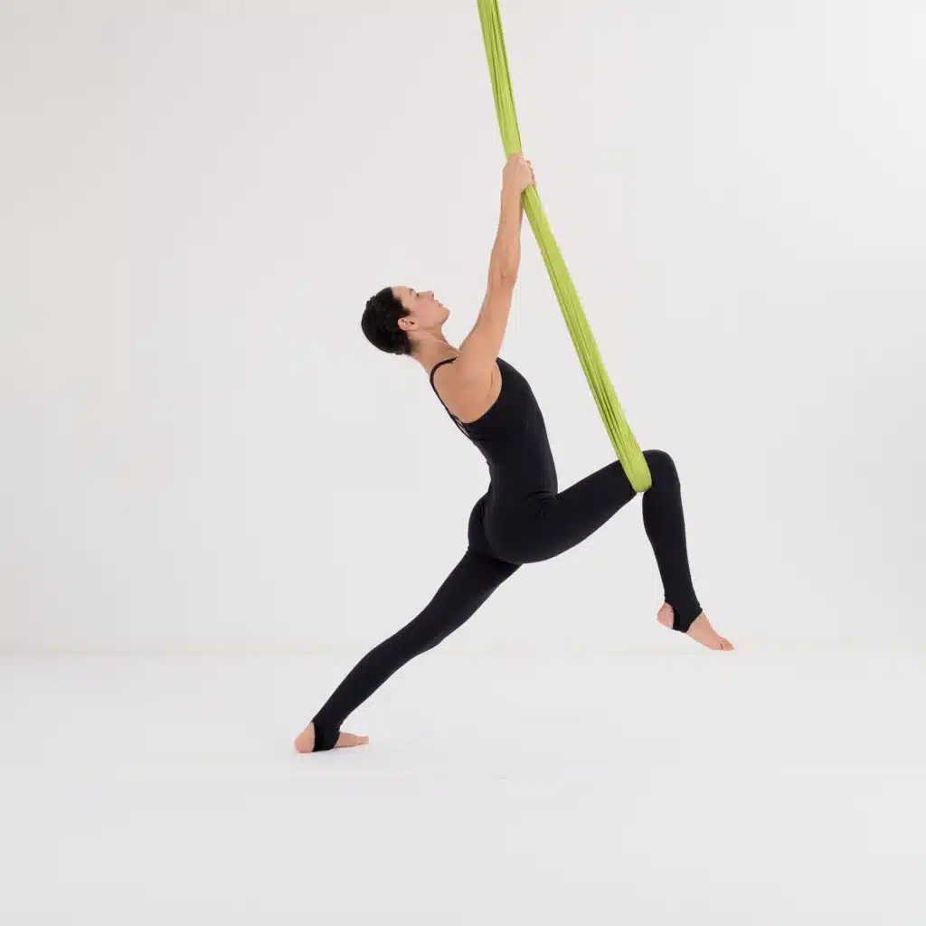 Krieger 2 im Aerial Yoga Tuch mit aufrechter Haltung und geöffnetem Brustraum zur Stärkung von Balance und Beinmuskulatur.