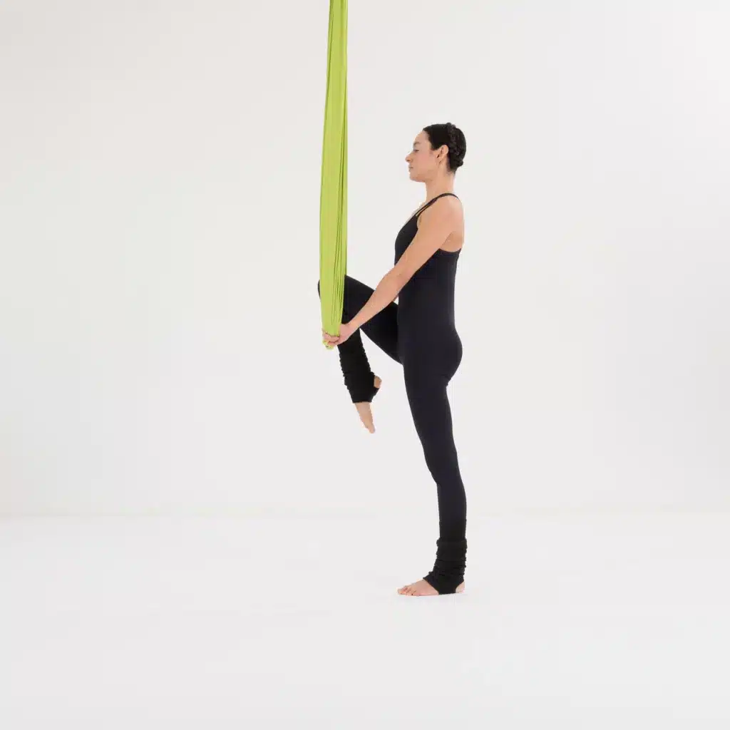 Aerial Yoga Standwaage dynamisch mit Knie zur Brust im grünen Tuch zur Kräftigung von Balance und Rumpf.