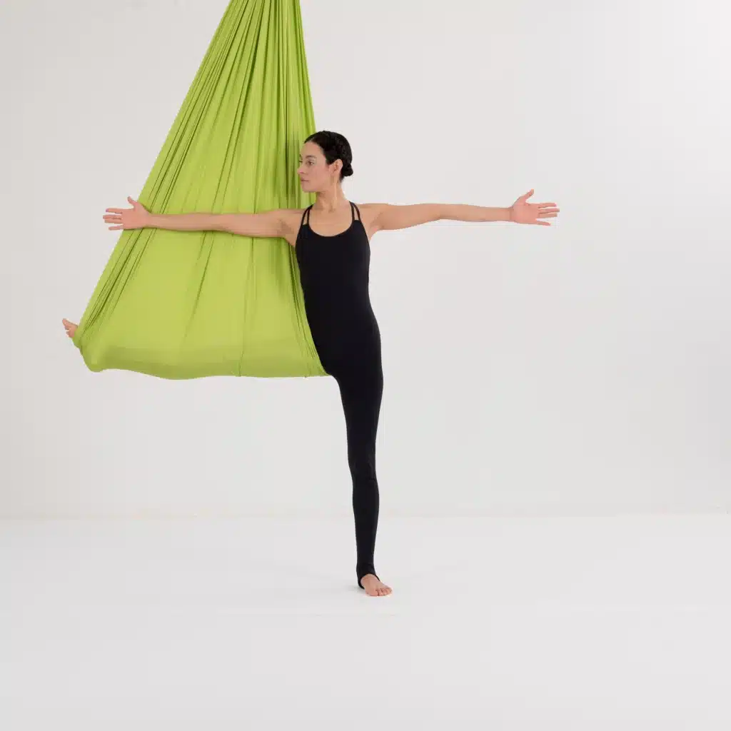 Aerial Yoga Twist im grünen Tuch mit ausgestreckten Armen zur Mobilisierung der Wirbelsäule und Öffnung des Oberkörpers.