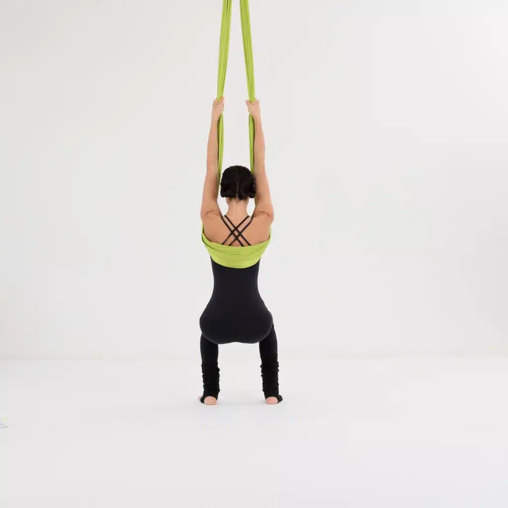 Aerial Yoga Stuhl Position im Aerial Yoga Tuch mit gestreckten Armen über dem Kopf. Rückenansicht der Übung zur Kräftigung von Schultern, Rücken und Beinen.