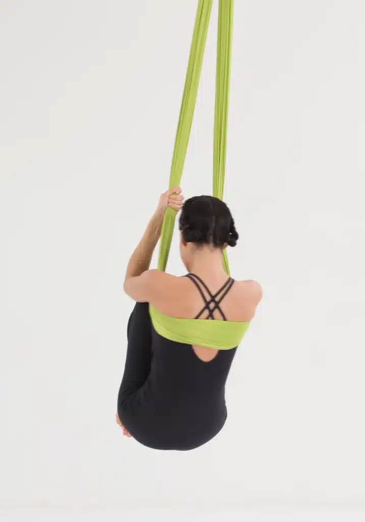 Aerial Yoga Core Übung im Aerial Yoga Tuch mit angezogenen Knien. Rückenansicht zur Aktivierung der Bauchmuskulatur und Stabilisierung des Körpers.