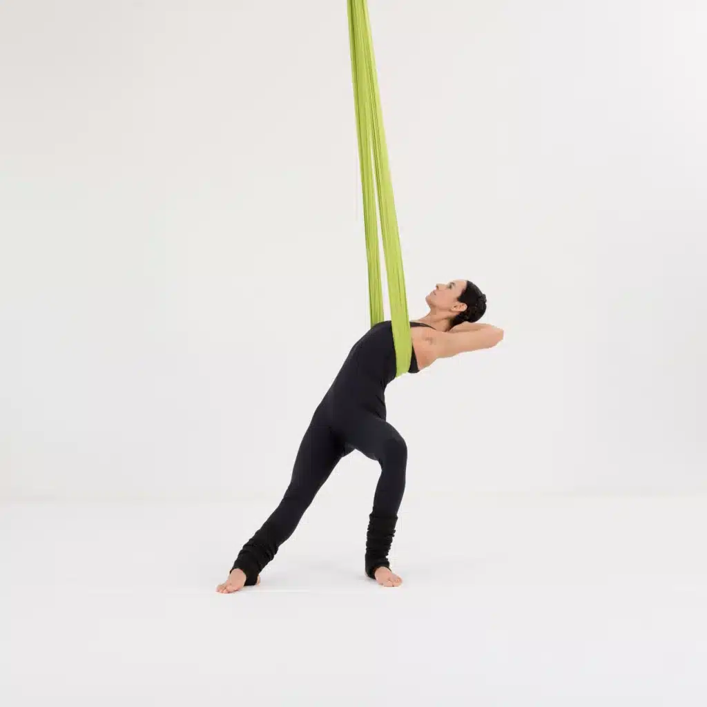 Aerial Yoga Twist aus der Stuhlposition im Aerial Yoga Tuch. Rückenrotation mit gebeugtem vorderen Bein zur Dehnung von Rücken, Schultern und Hüften.