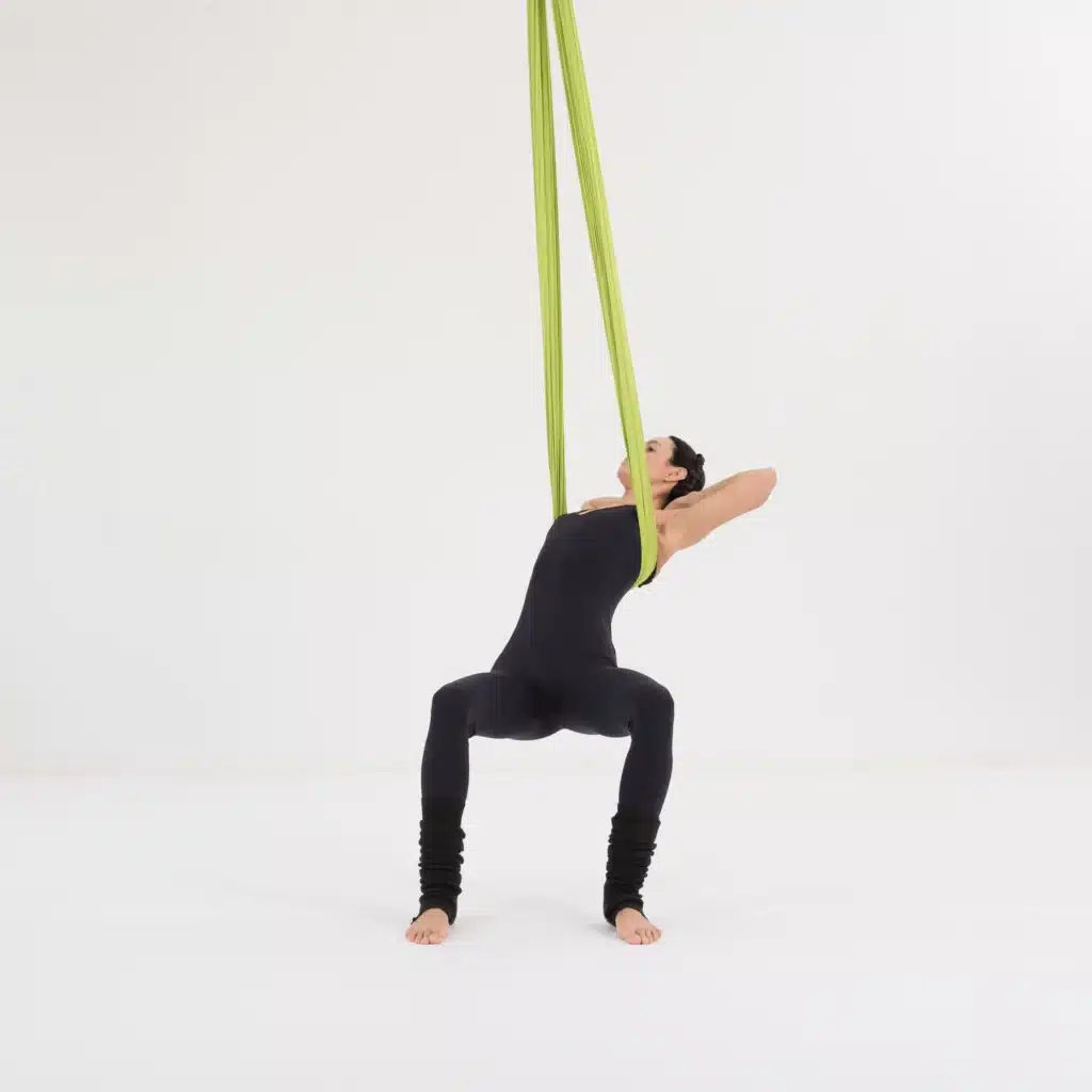 Aerial Yoga Twist und Rückenöffnung im Aerial Yoga Tuch. Frau lehnt sich in einer Stuhlposition nach hinten und öffnet Brust und Schultern im Yoga Hammock.
